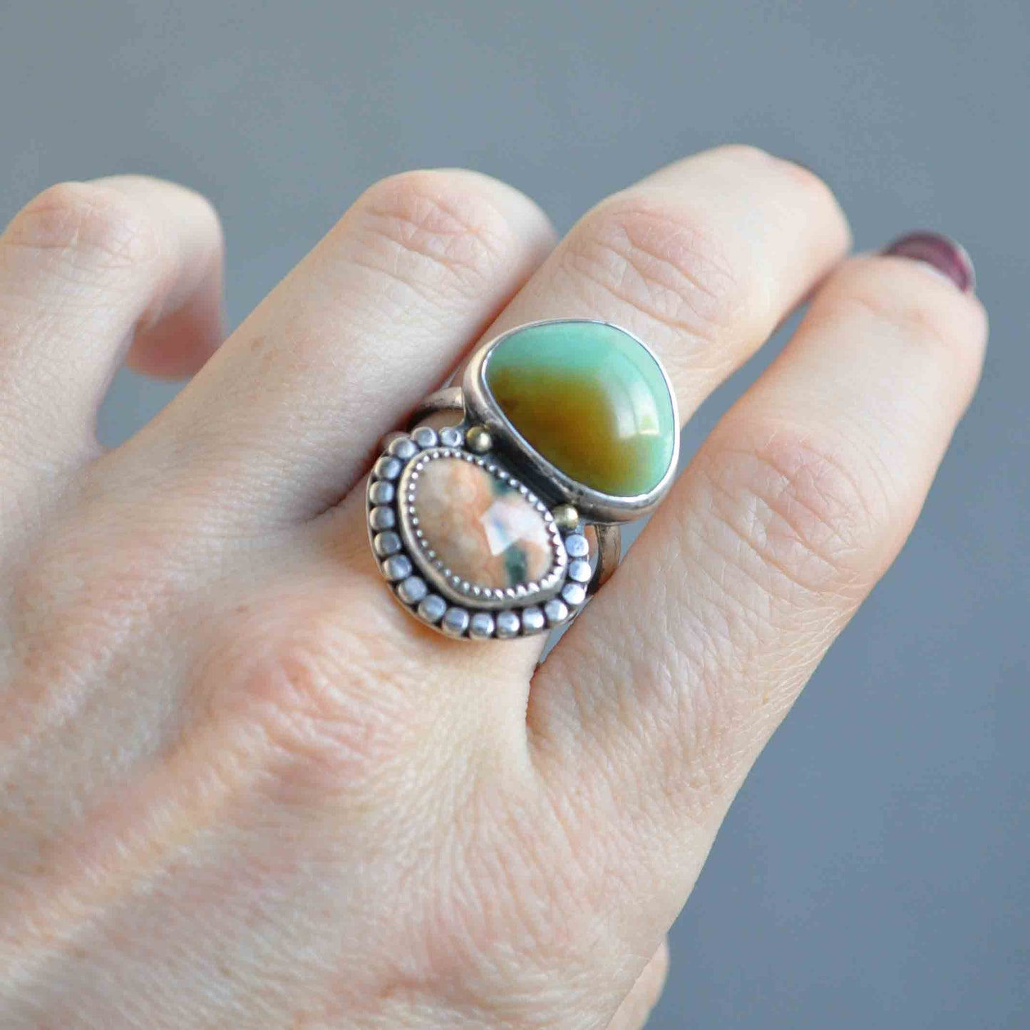 Hand wearing a silver ring with a green stone against a gray background