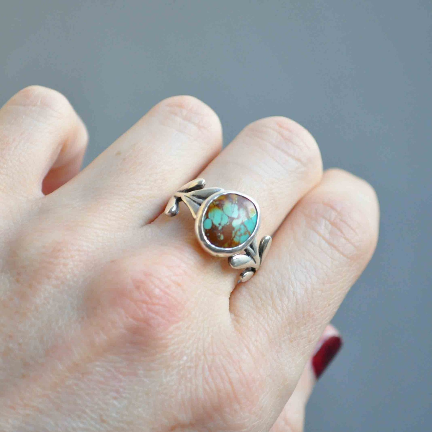 Silver ring with a turquoise stone on a finger against a gray background