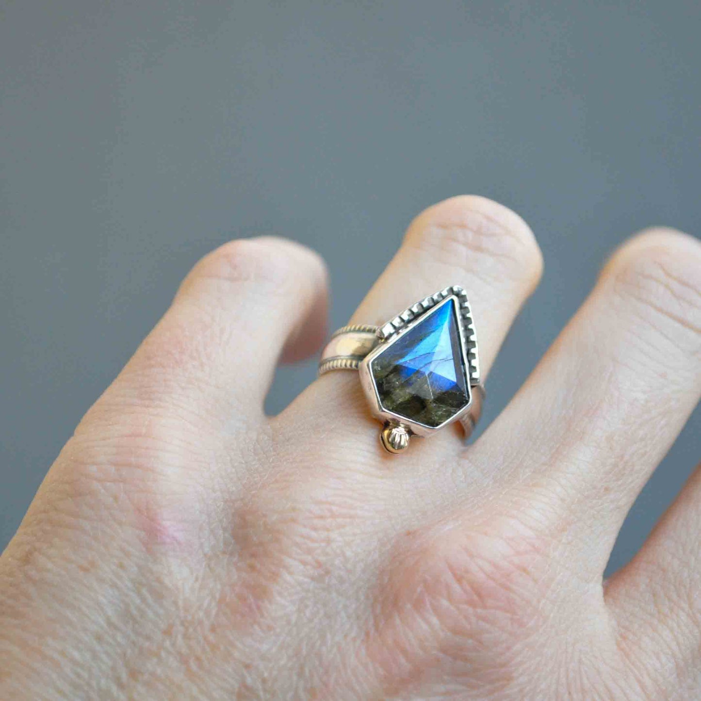 Hand wearing a ring with a large, faceted gemstone on a gray background
