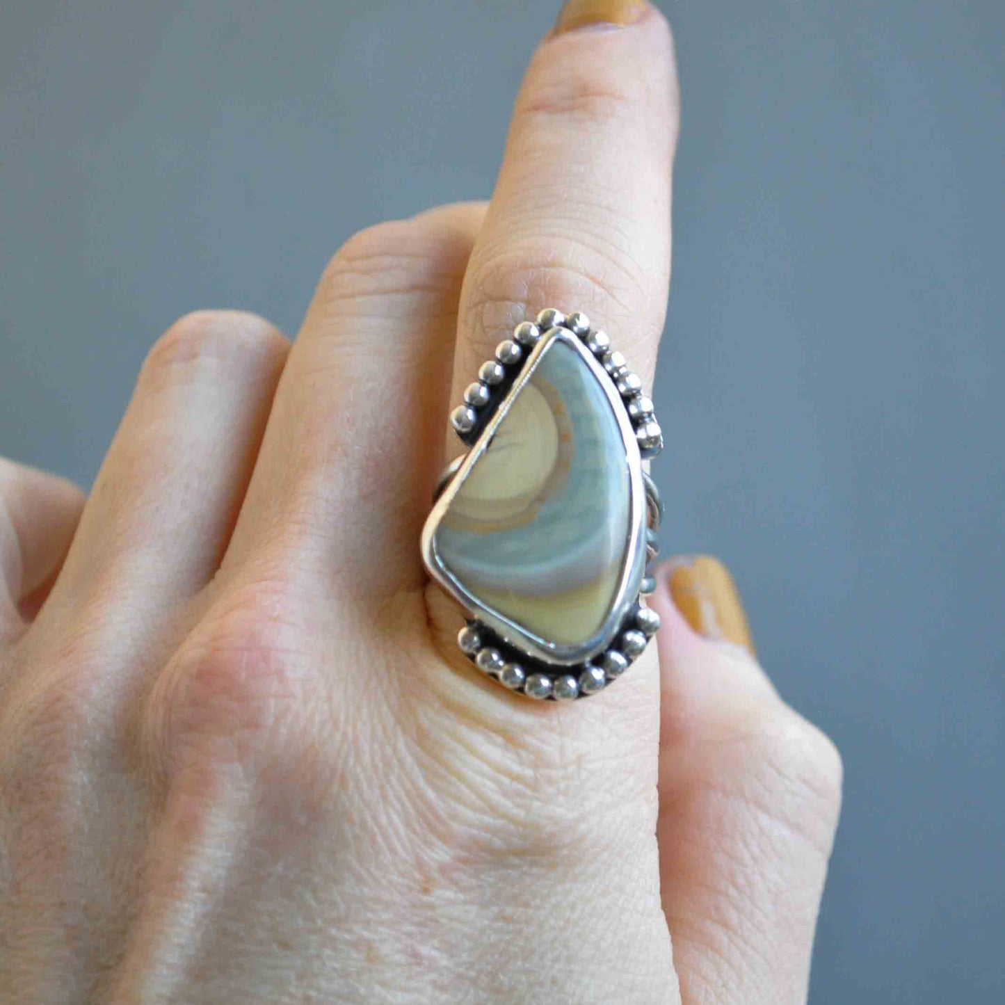 Hand wearing a large, decorative ring with a teardrop-shaped stone against a neutral background