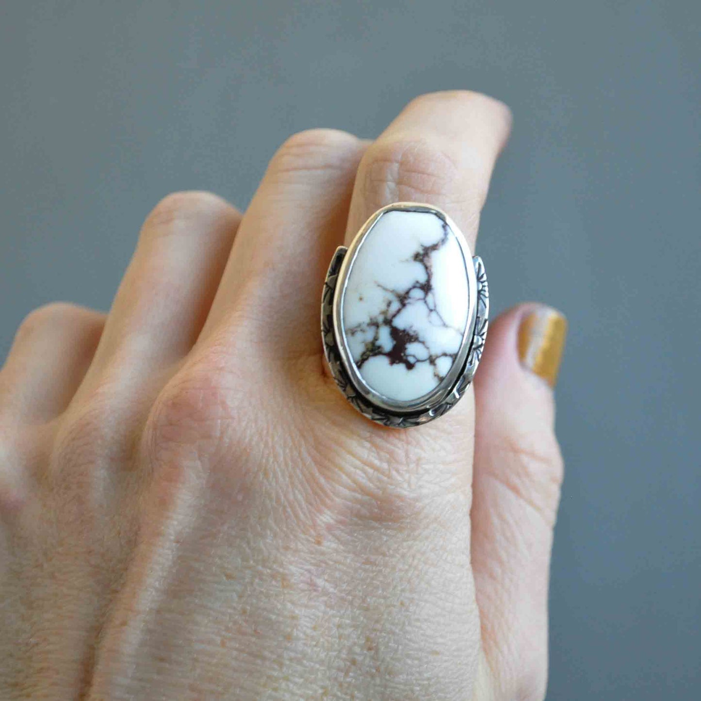 Hand wearing a ring with a large white stone on a gray background