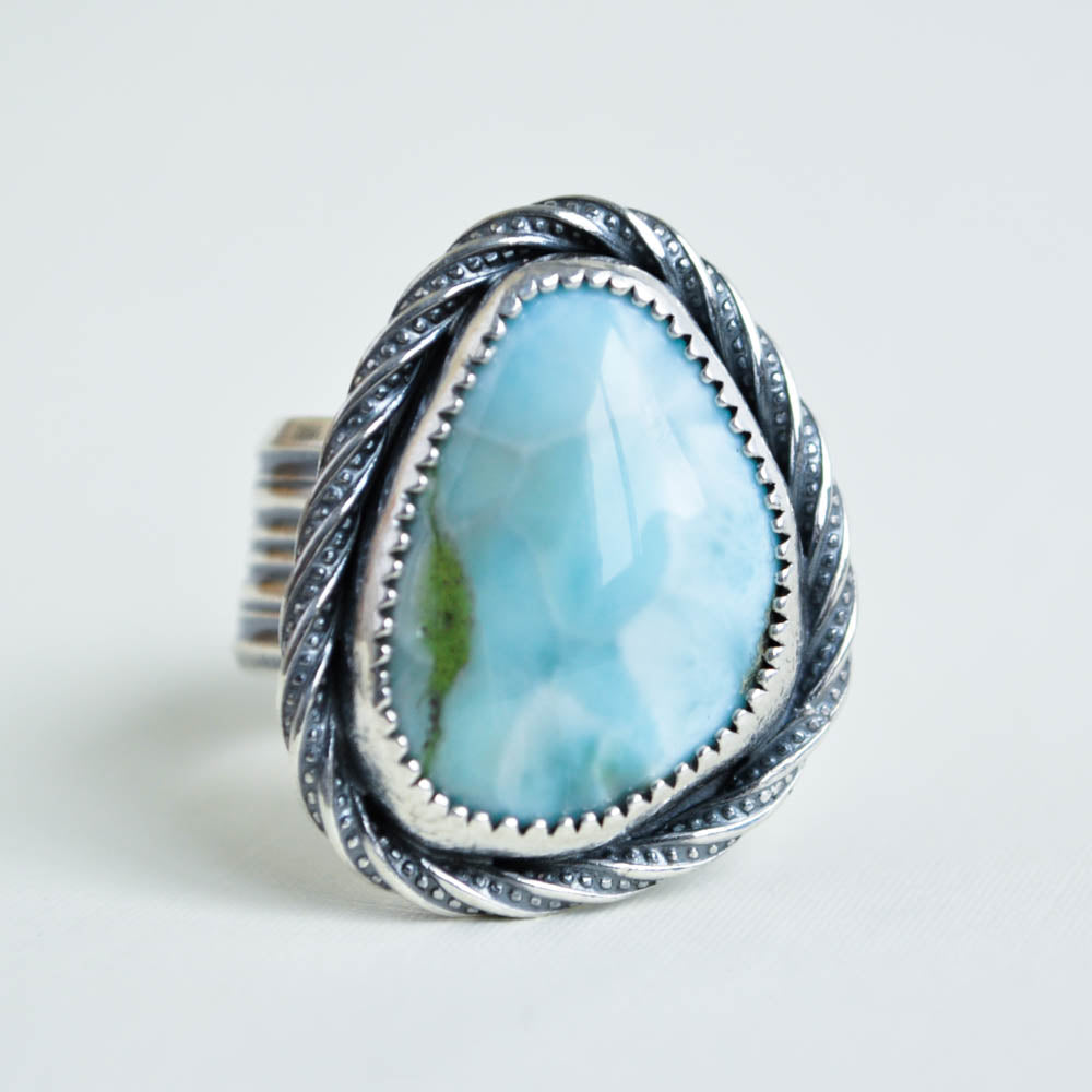A light blue and white smooth larimar cabochon set in sterling silver with a twist patterned border and a wide ridged band.