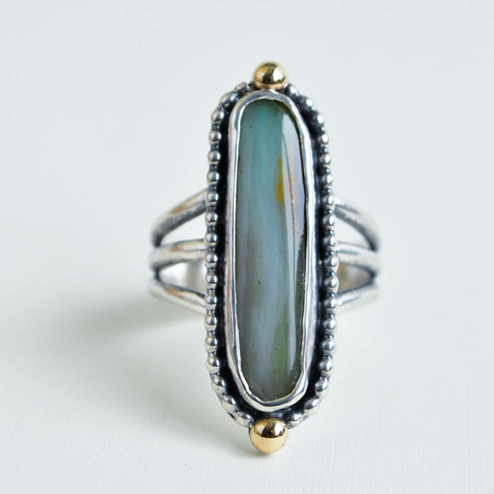 An oblong, smooth oval shaped, green peruvian opal cabochon with 14k yellow gold beads at the top and bottom. Solid sterling silver on a triple split band.