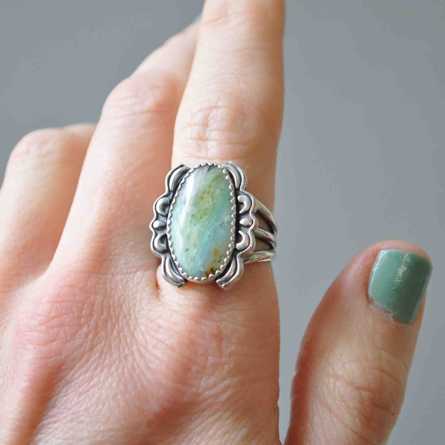 Silver ring with a turquoise stone on a finger against a neutral background