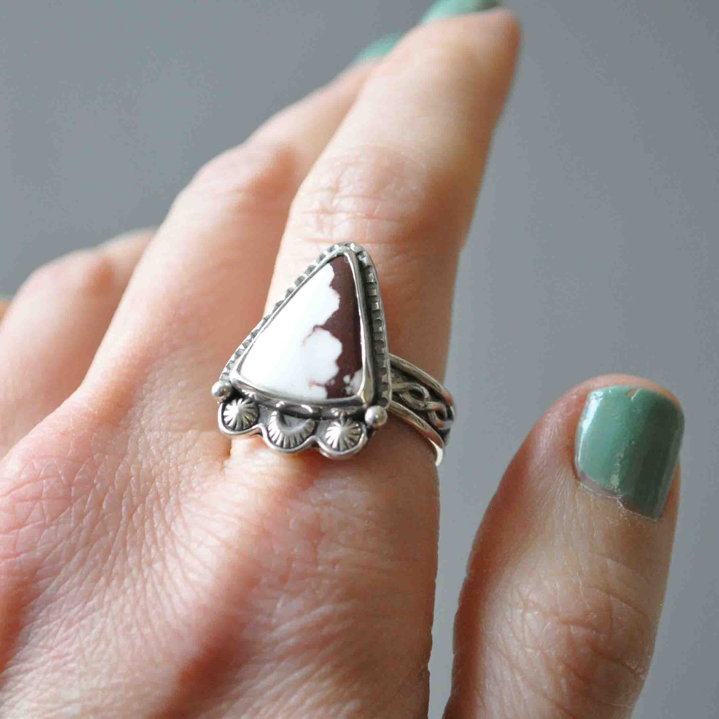 Silver ring with a large stone on a finger against a neutral background