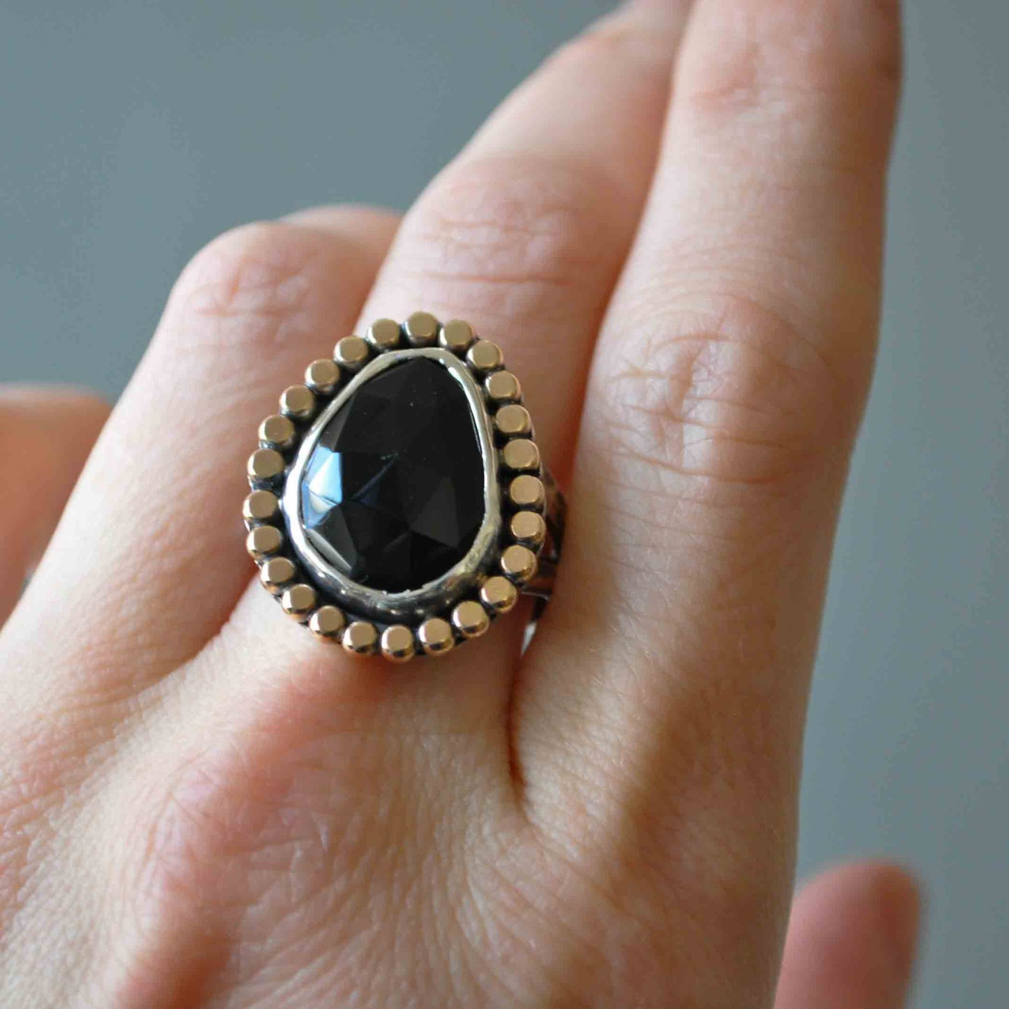 Ring with a black stone and gold accents on a finger against a neutral background
