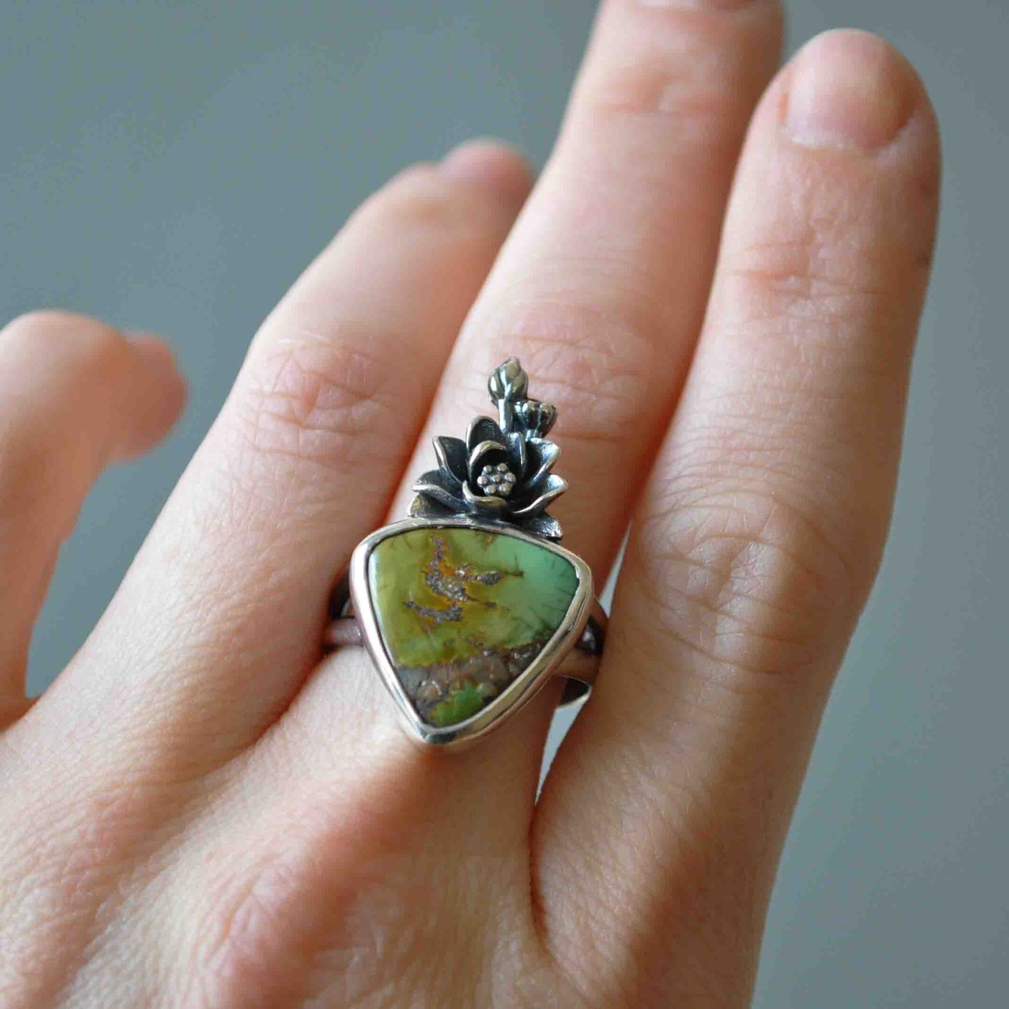 Hand wearing a ring with a green stone and silver design on a neutral background