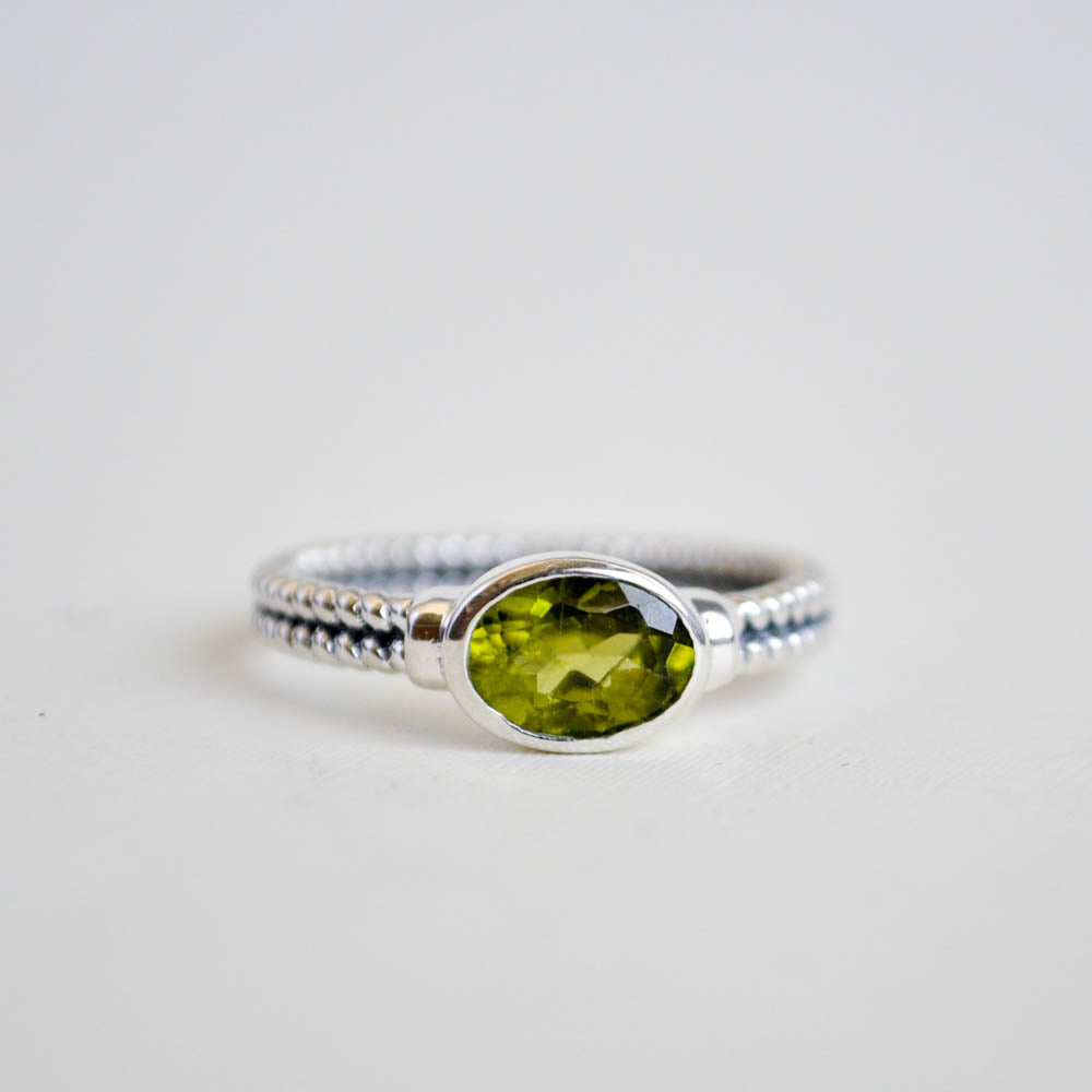 Green oval peridot gemstone bezel set horizontally on a double twist sterling silver ring band.