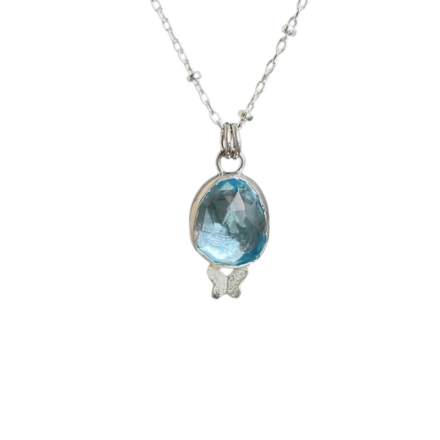 Faceted light blue topaz gemstone bezel set in sterling silver and paired with a tiny butterfly embellishment underneath. Solid sterling silver setting and chain.
