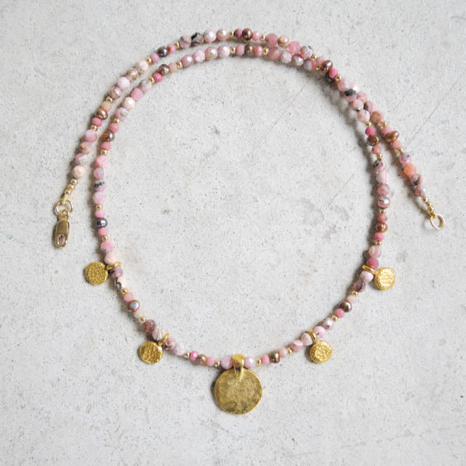 Rhodochrosite beaded necklace with gold coins on a textured surface