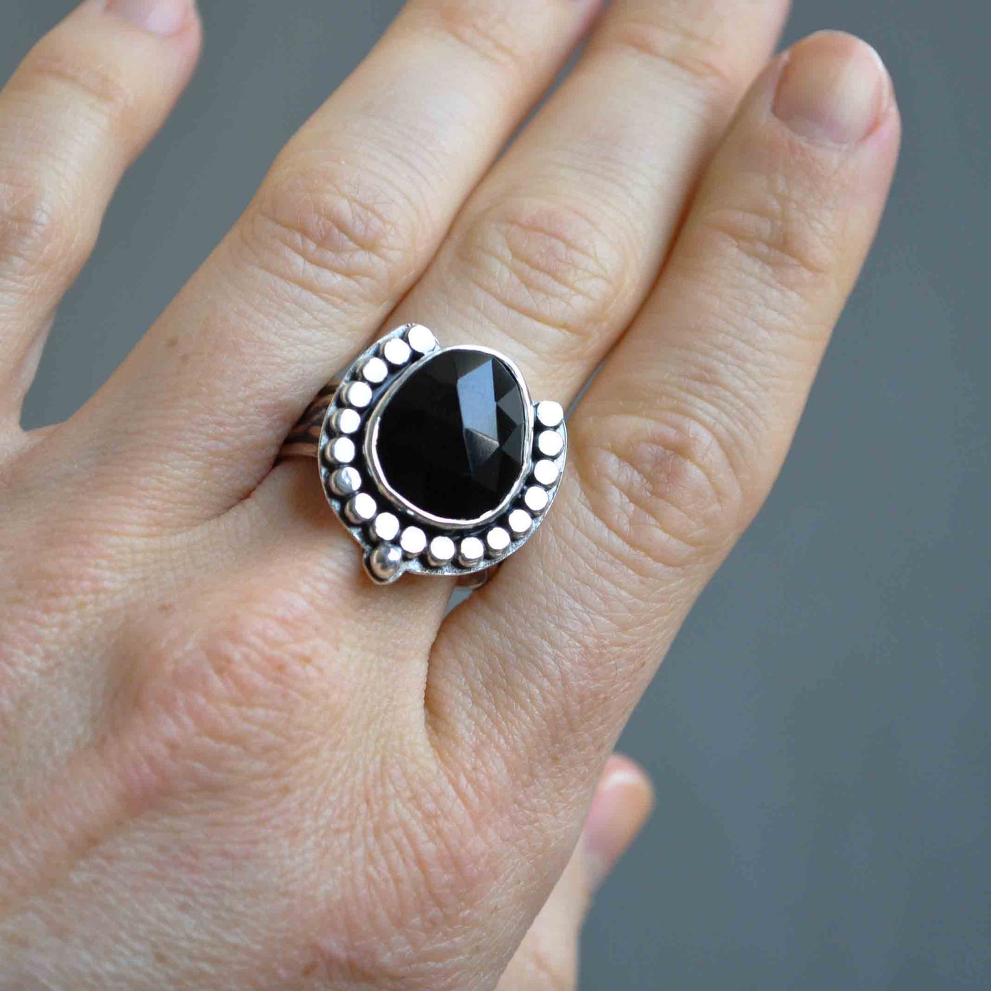 Silver ring with a black gemstone on a hand against a gray background