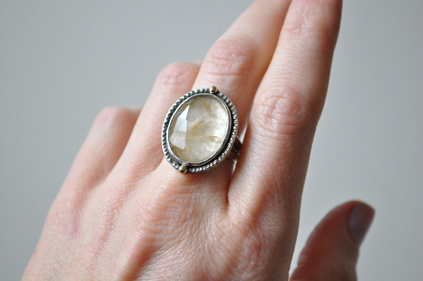 Ring with a large stone on a person's finger against a neutral background