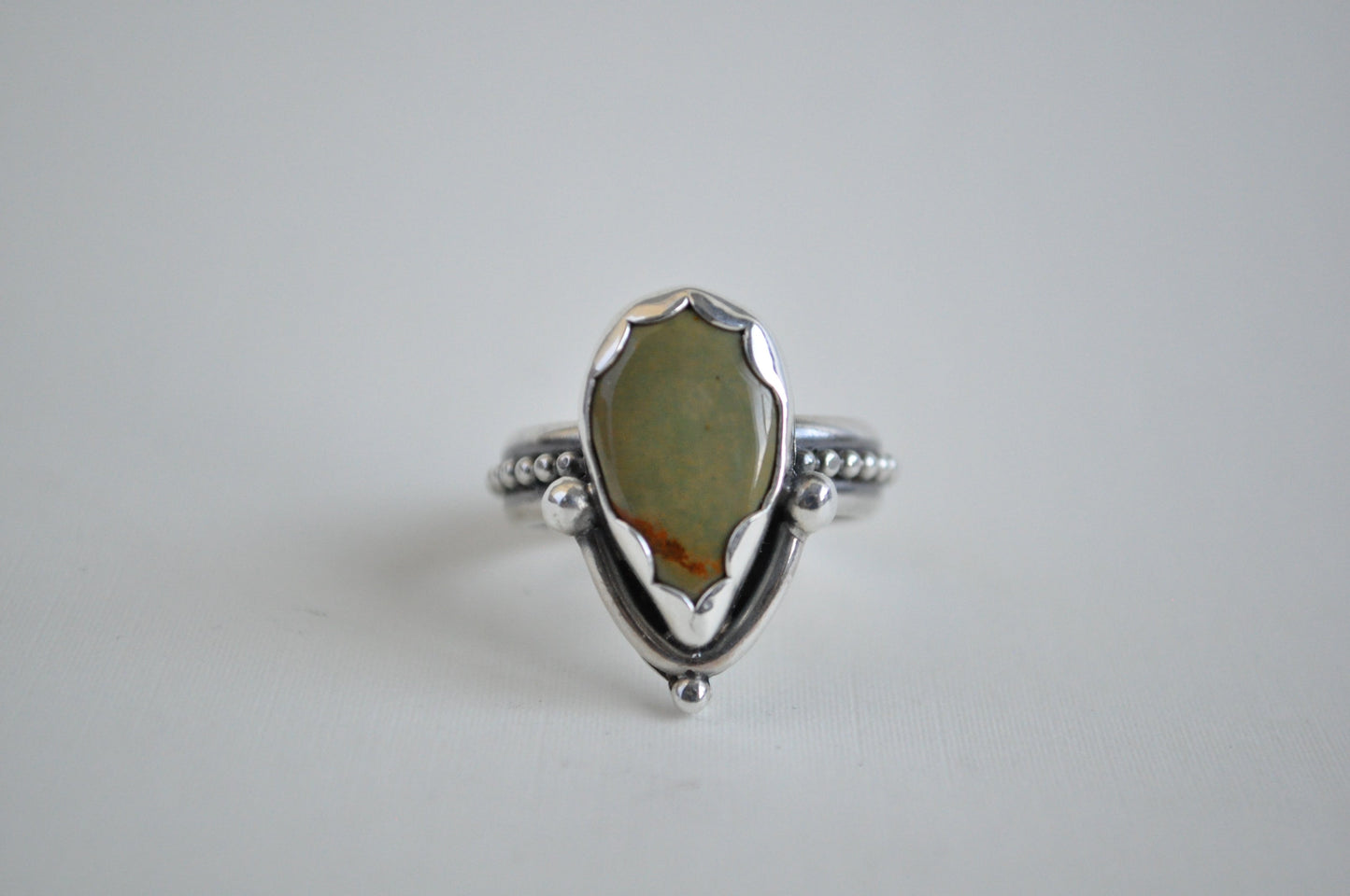 A sage green turquoise set in sterling silver with a scalloped bezel and a beaded band.