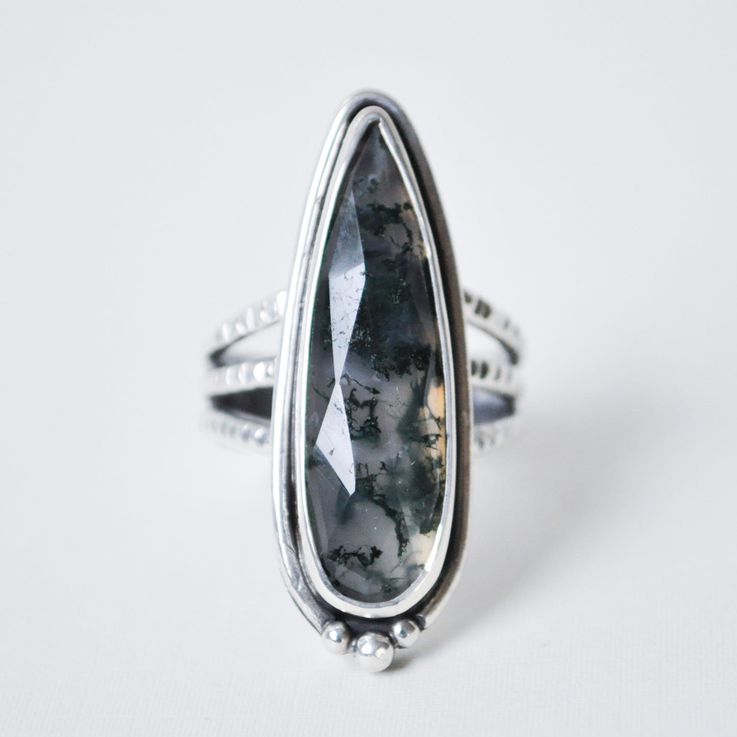 Silver ring with a large, teardrop-shaped black stone on a light gray background