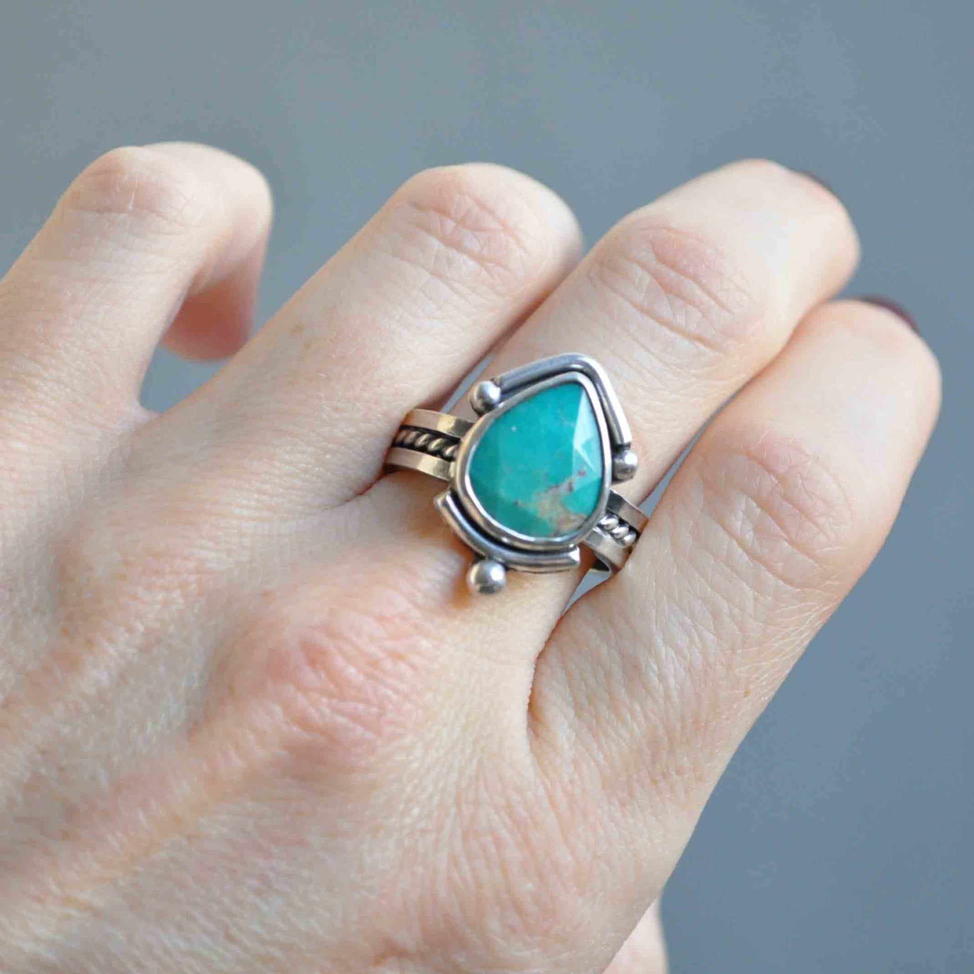 Turquoise ring on a finger against a gray background