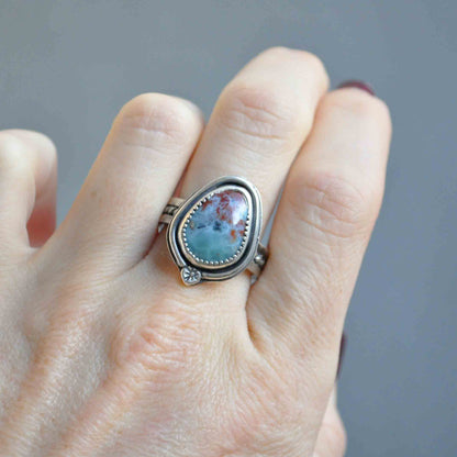 Silver ring with a turquoise stone on a finger against a gray background