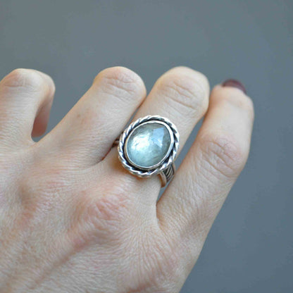Silver ring with a gemstone on a finger against a gray background