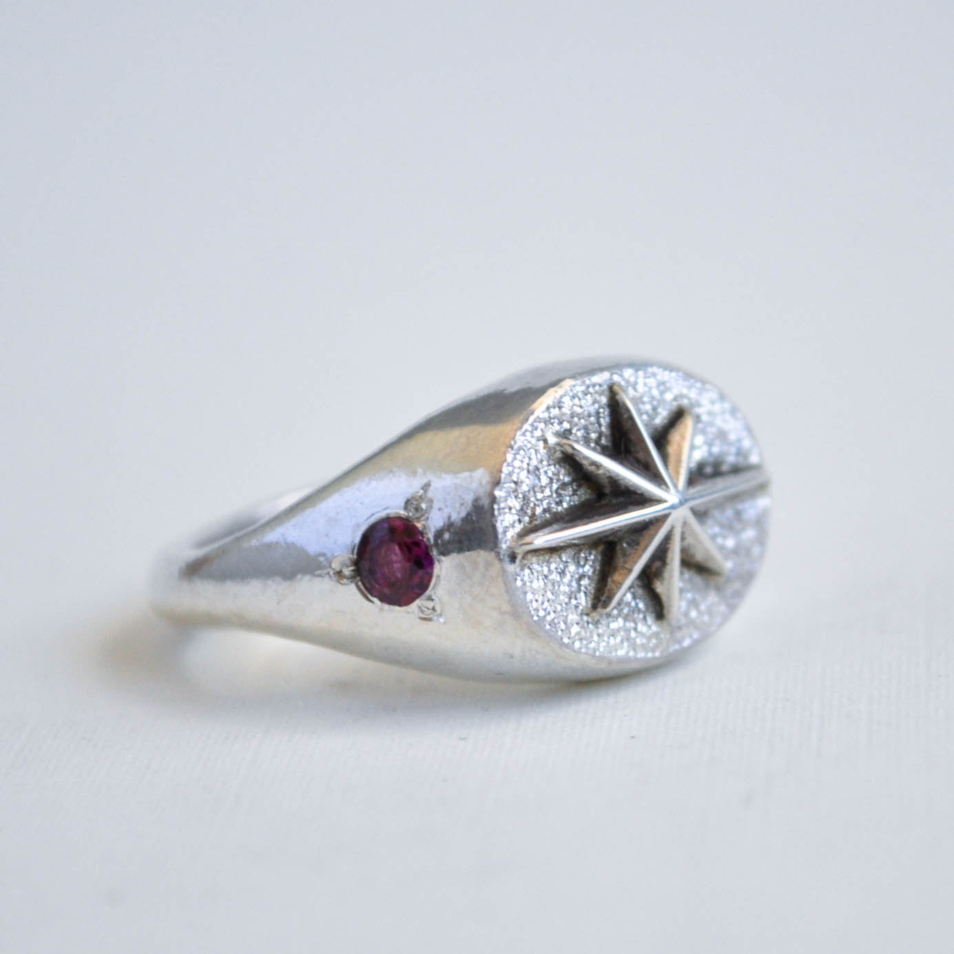 Silver ring with star design and red gemstone on a light gray background