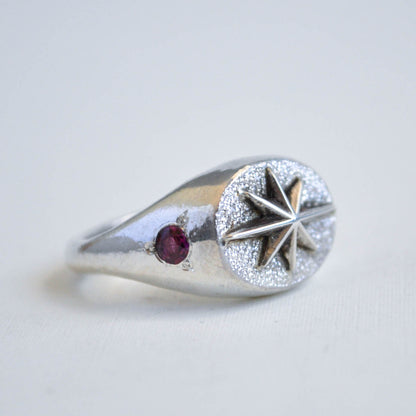 Silver ring with star design and red gemstone on a light gray background