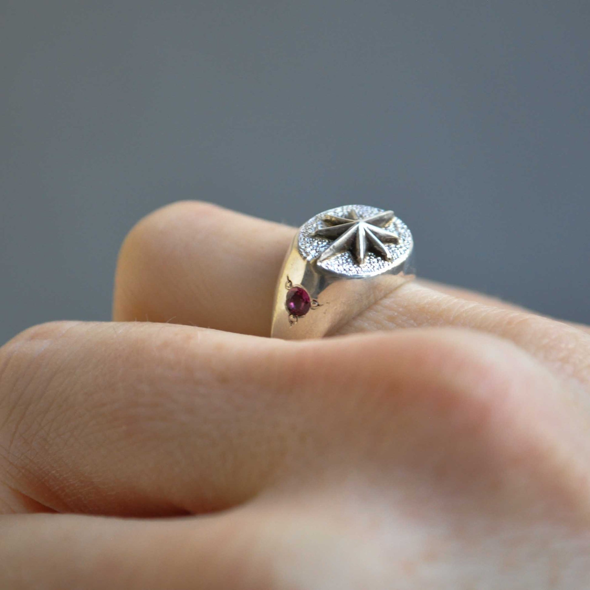 Close-up of a hand wearing a decorative ring with a red gemstone on a gray background