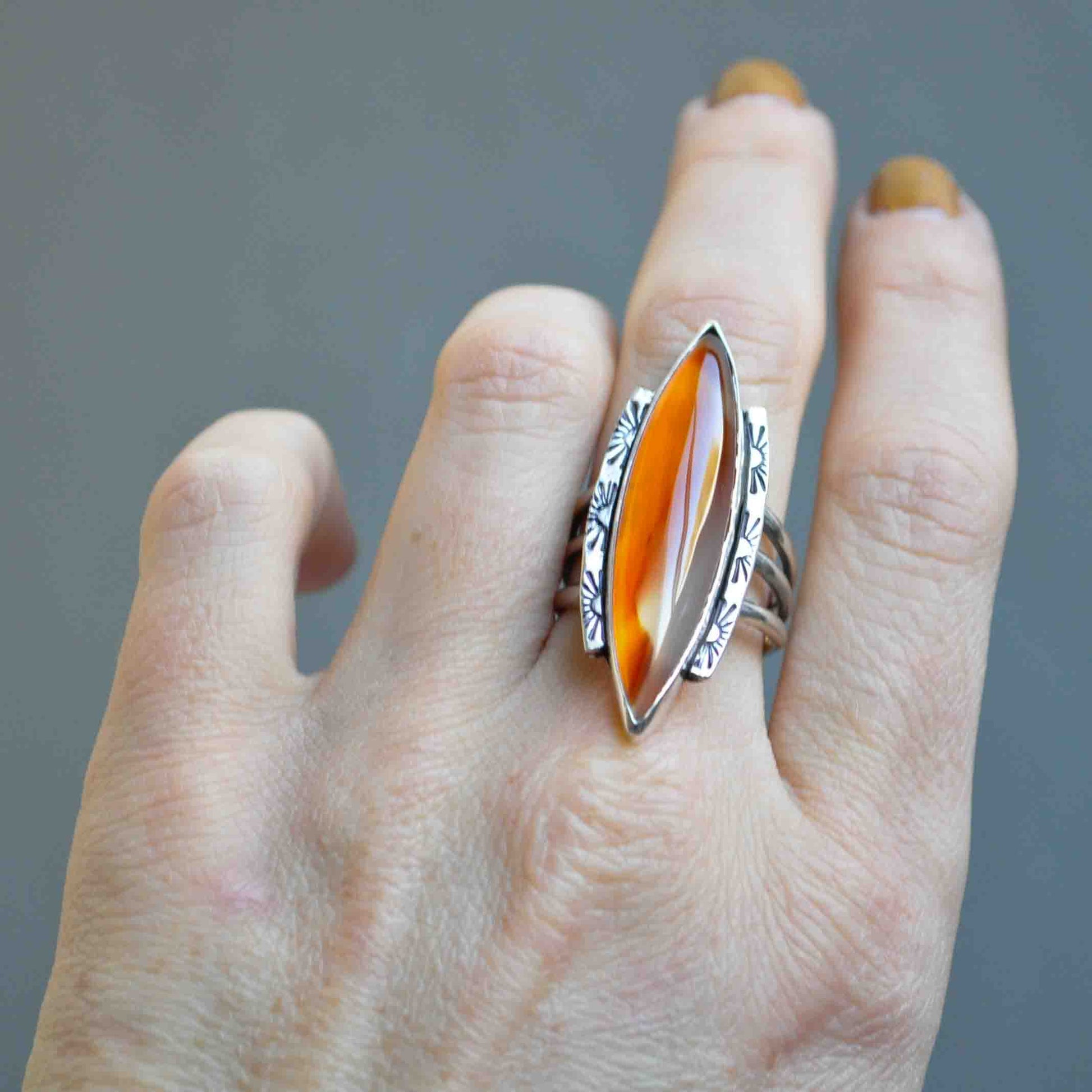 Hand wearing a silver ring with an orange stone on a gray background