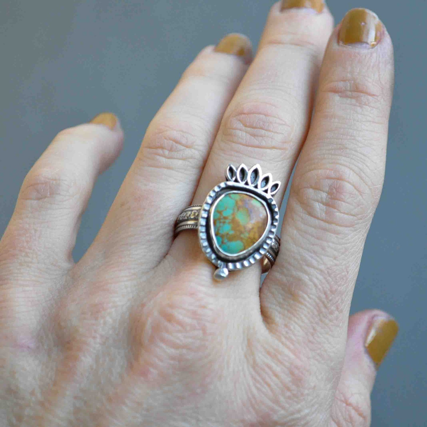 Hand wearing a silver ring with a turquoise stone against a gray background