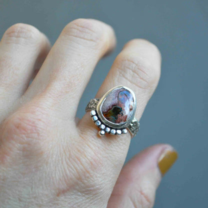 Silver ring with a colorful stone on a finger against a gray background