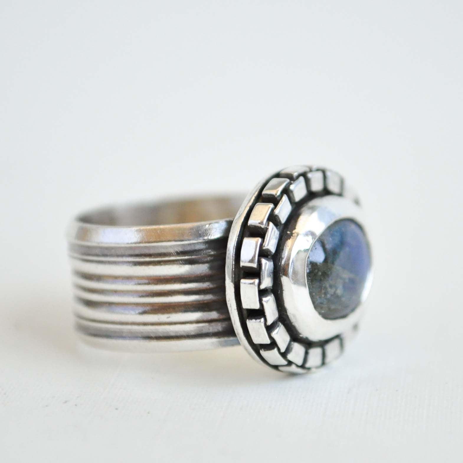 Silver ring with textured band and circular design on a white background
