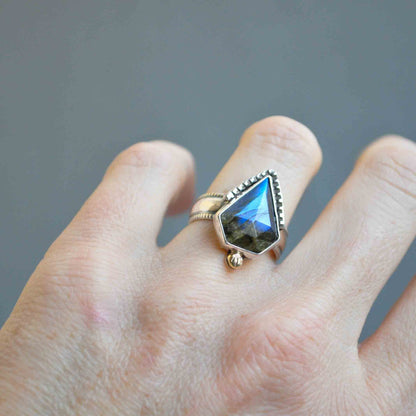 Hand wearing a ring with a large, faceted gemstone on a gray background