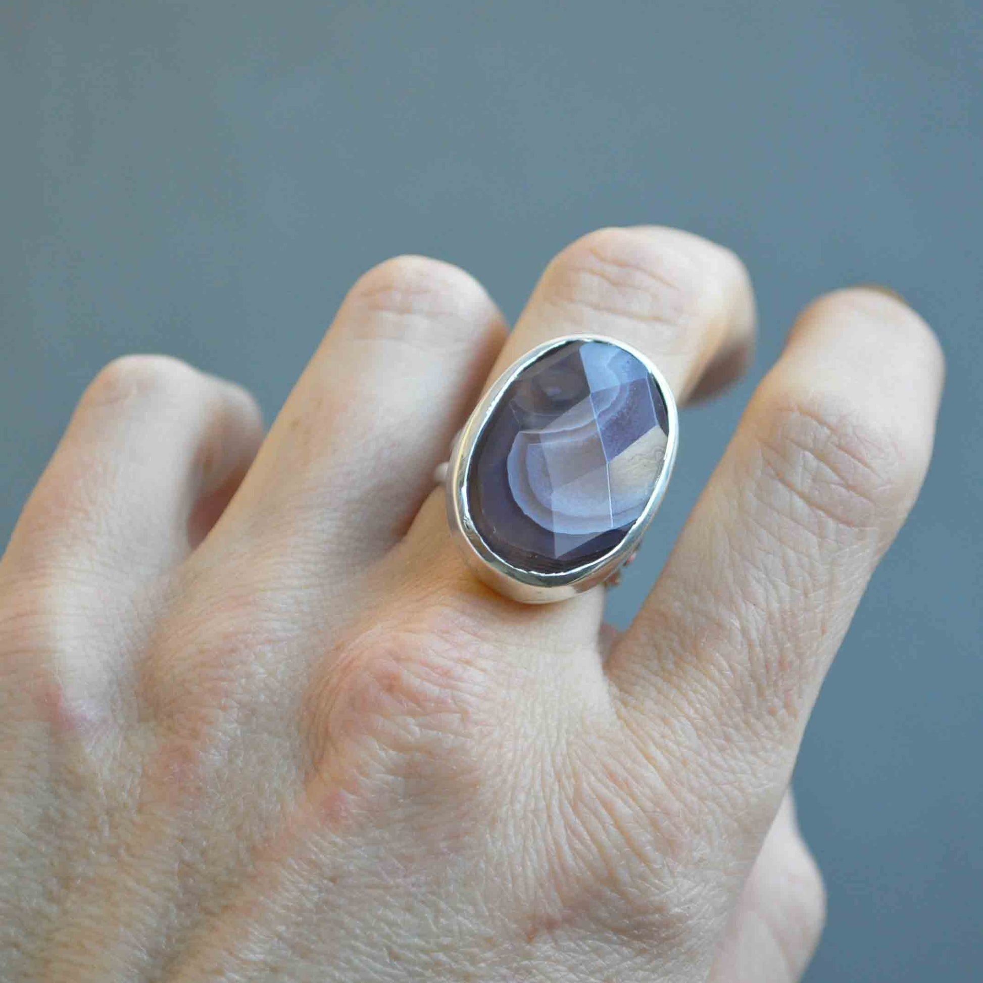 Hand wearing a ring with a purple stone on a gray background