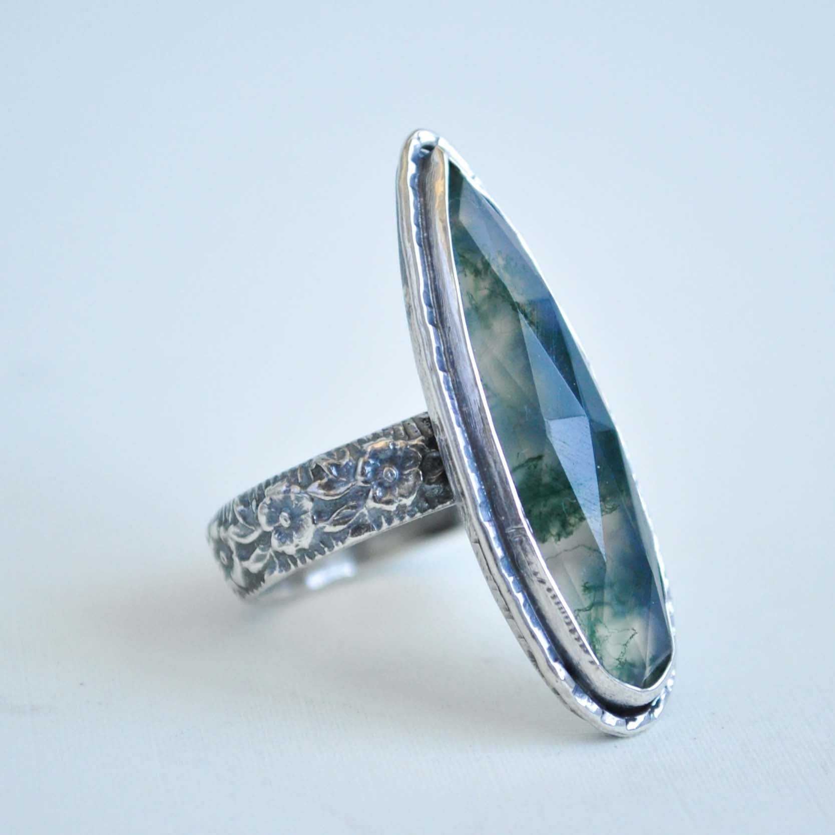 Silver ring with a large moss quartz gemstone on a light gray background