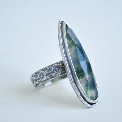 Silver ring with a large moss quartz gemstone on a light gray background
