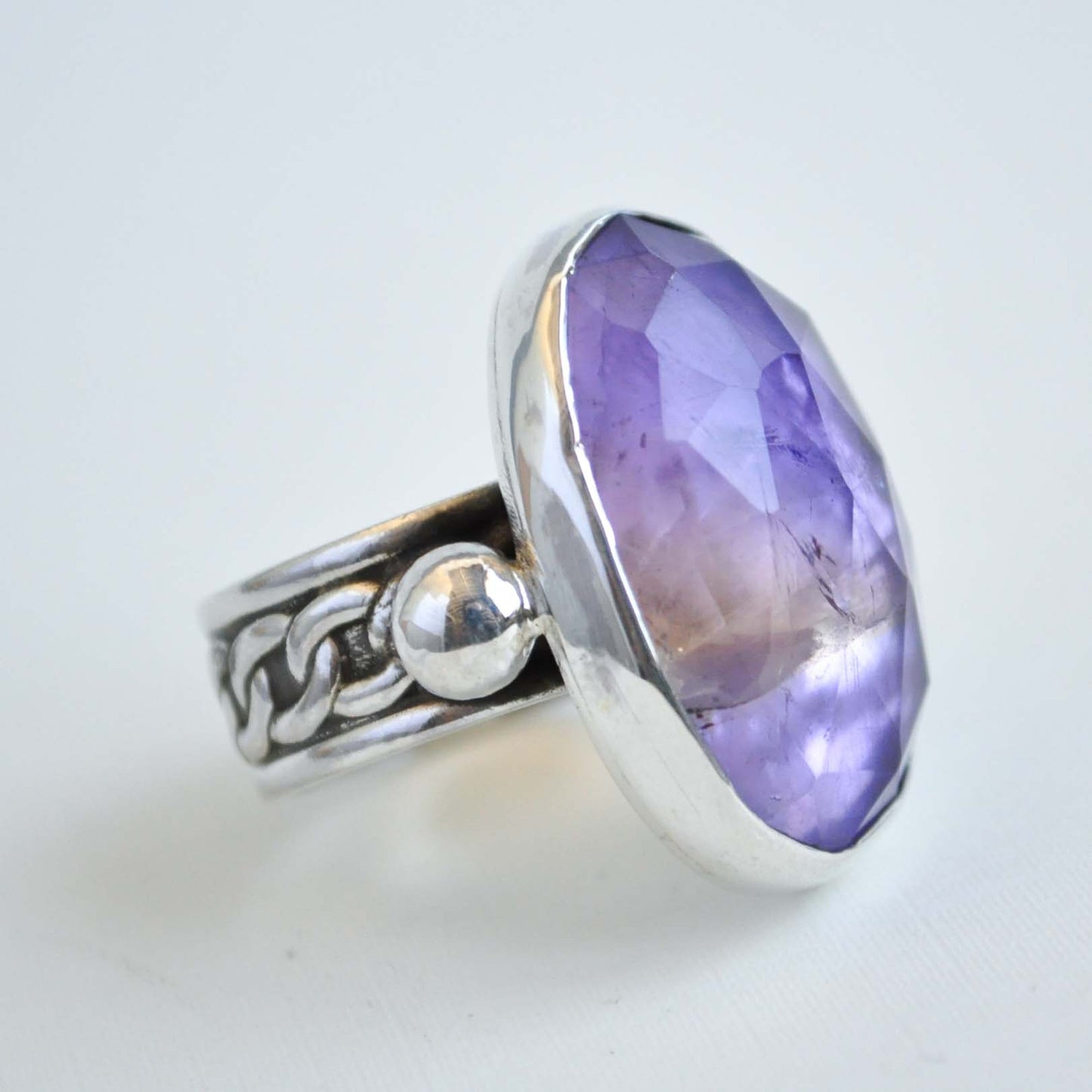 Silver ring with a large purple gemstone on a light gray background