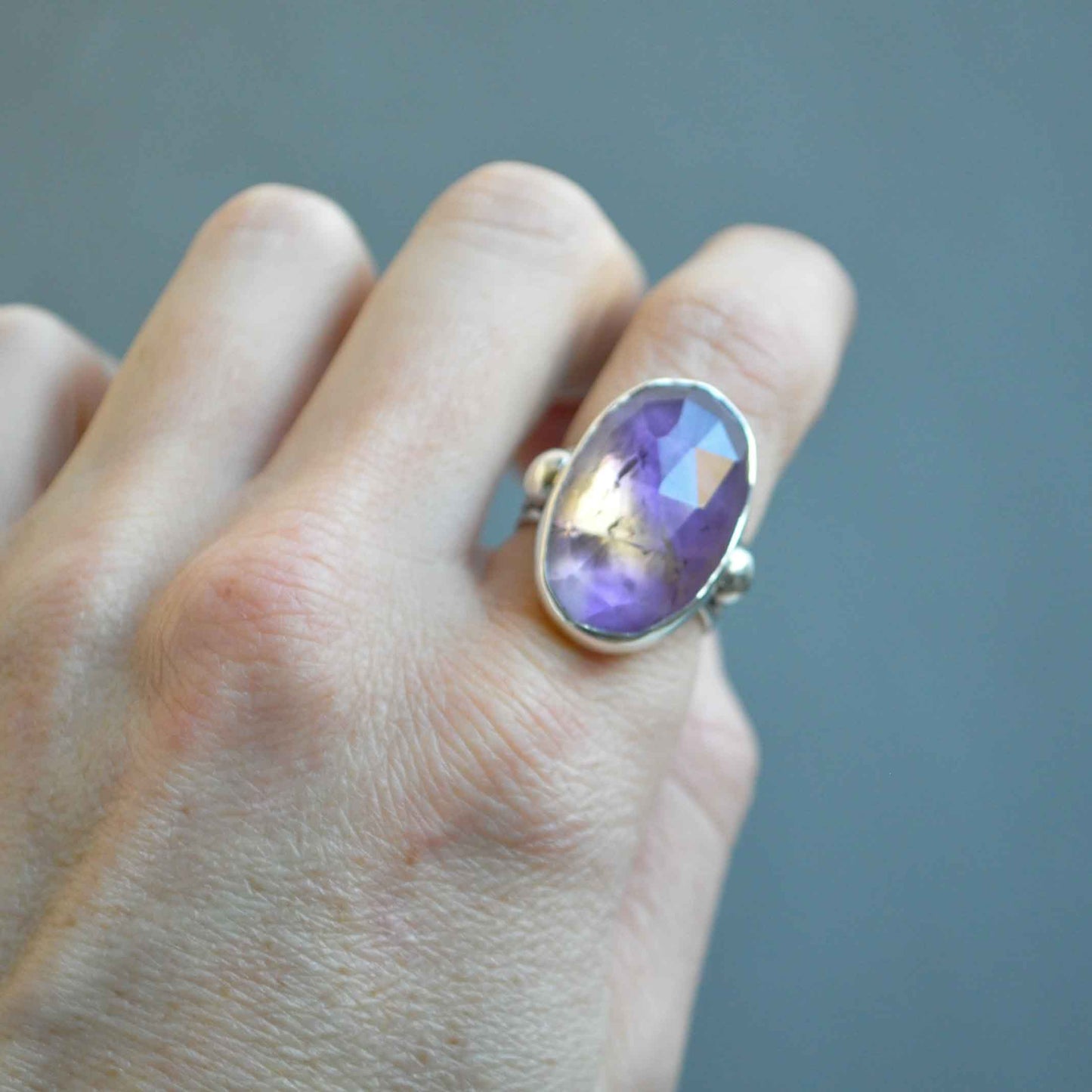 Hand wearing a ring with a purple gemstone on a neutral background