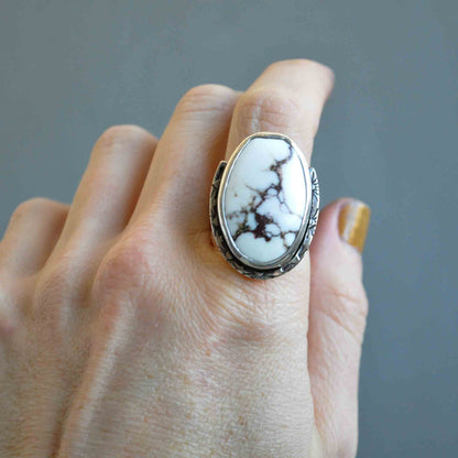 Hand wearing a ring with a large white stone on a gray background
