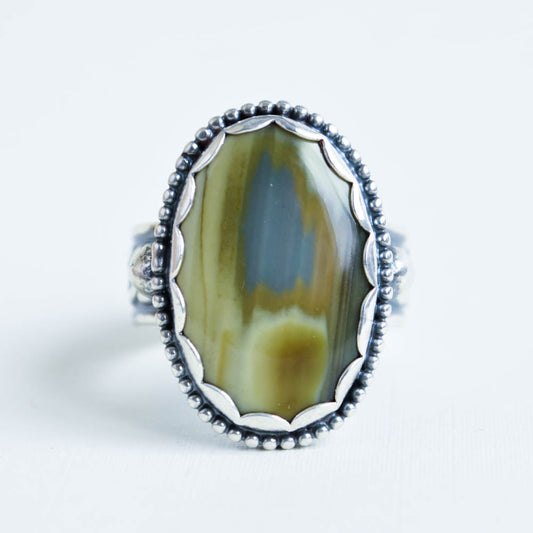A green-blue Imperial Jasper gemstone with a scalloped bezel and beaded border on a chain pattern band.