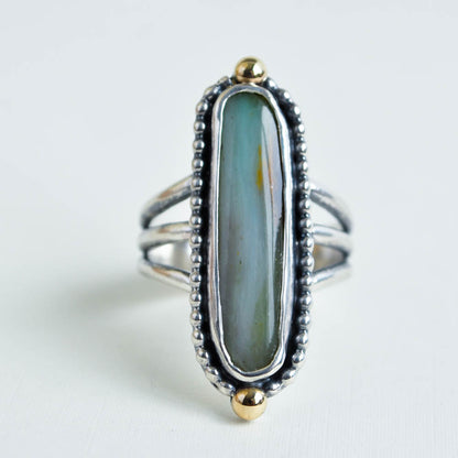 An oblong, smooth oval shaped, green peruvian opal cabochon with 14k yellow gold beads at the top and bottom. Solid sterling silver on a triple split band.