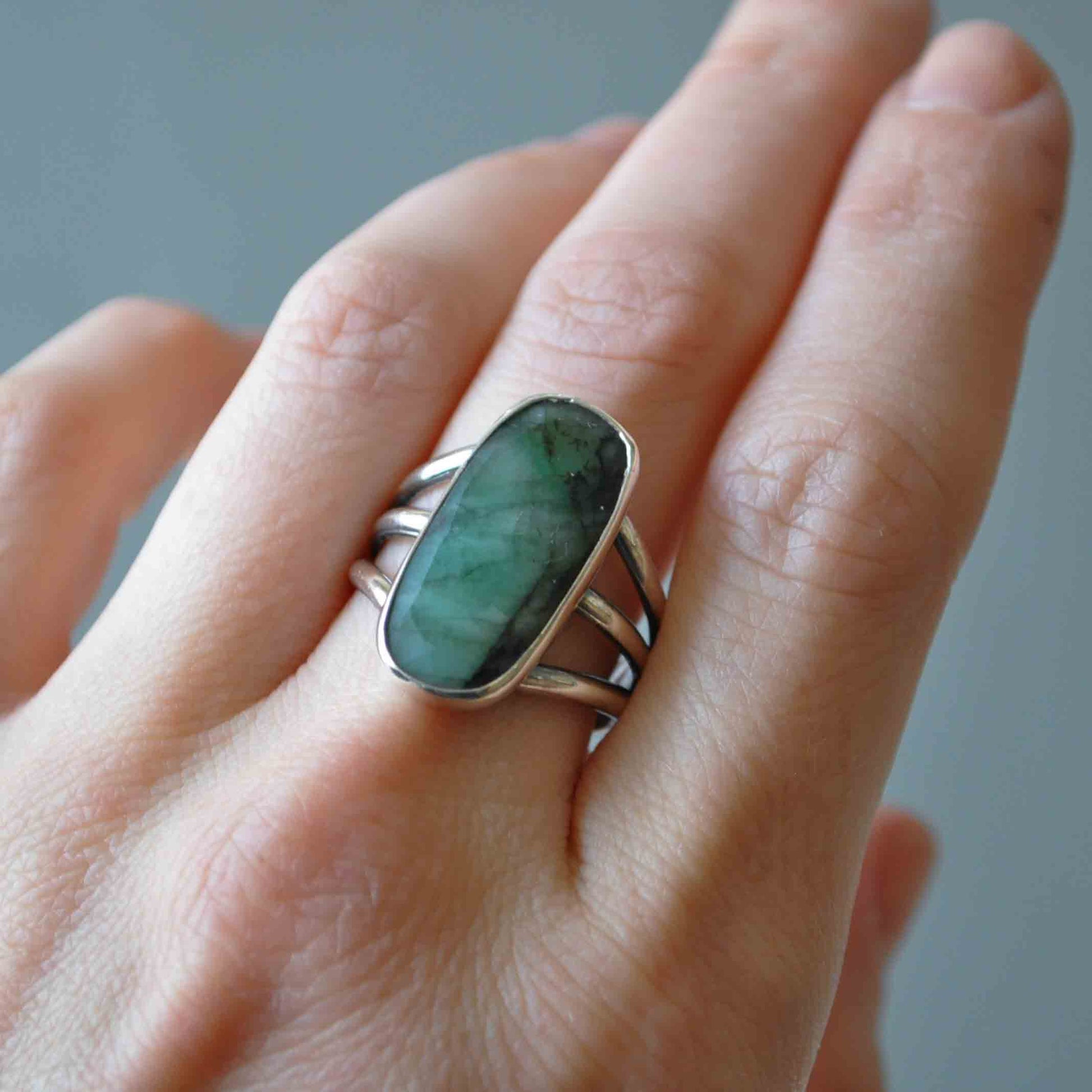 Hand wearing a silver ring with a green stone against a neutral background