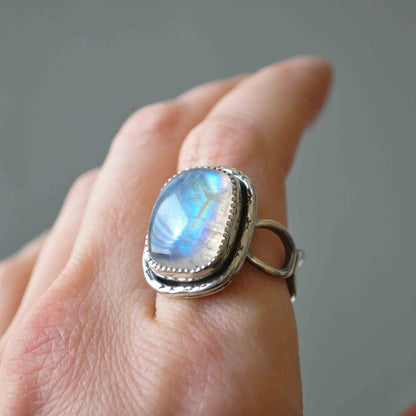 Silver ring with a rainbow moonstone on a hand against a gray background