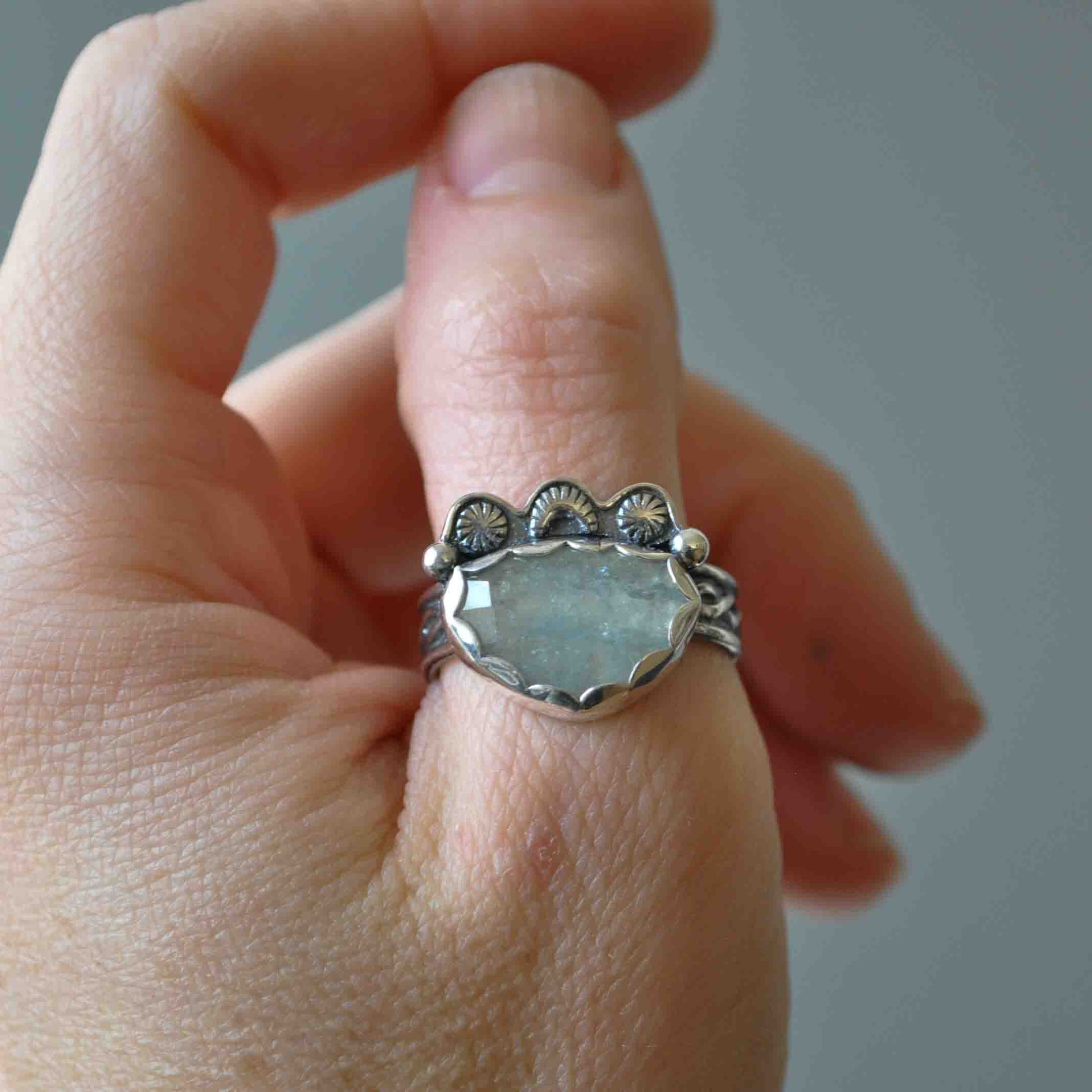 Silver ring with a large gemstone on a person's finger against a neutral background