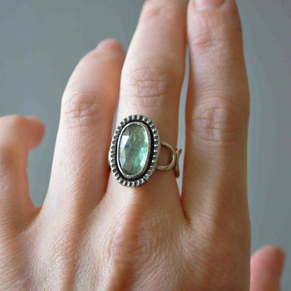 Hand wearing a ring with a green gemstone on a neutral background