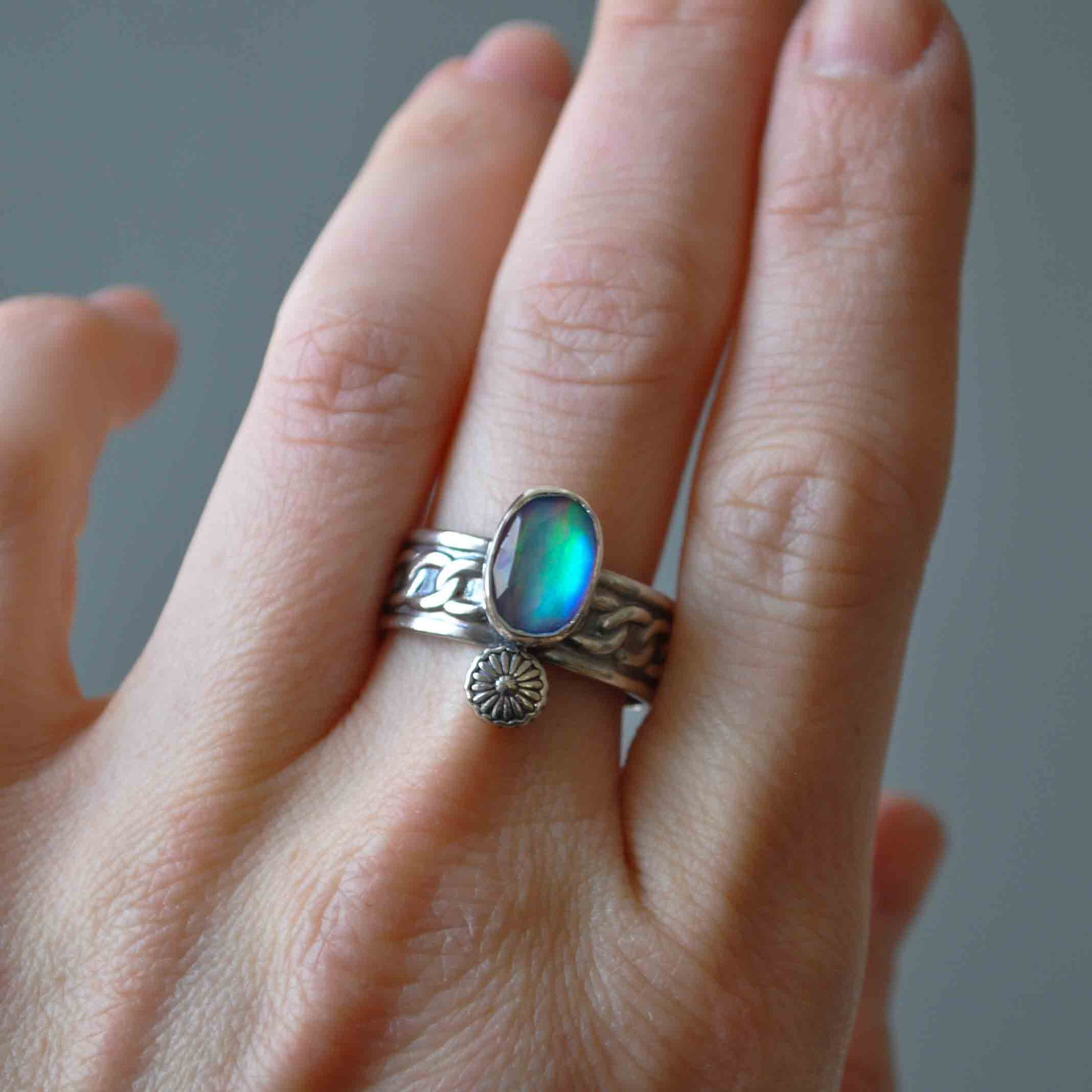 Hand wearing a silver ring with a blue gemstone on a neutral background