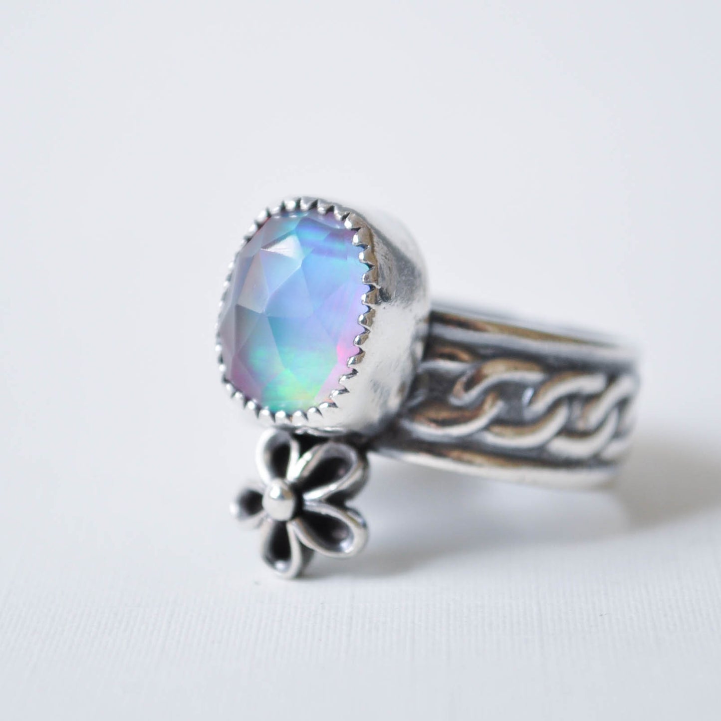 Silver ring with a colorful gemstone and floral charm on a white background