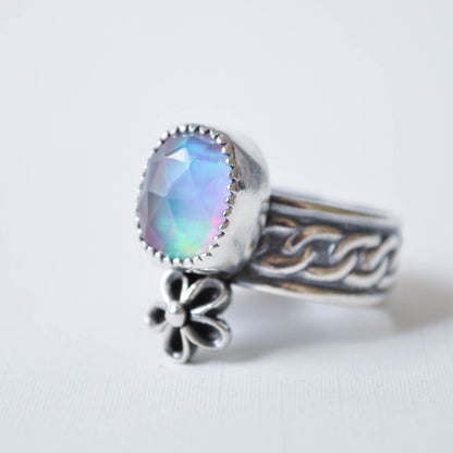 Silver ring with a colorful gemstone and floral charm on a white background