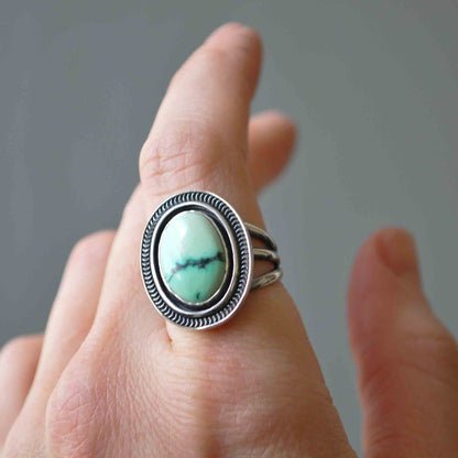 Silver ring with a turquoise stone on a finger against a neutral background