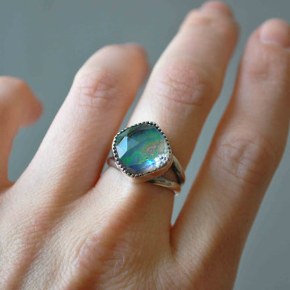 Ring with a green gemstone on a person's finger against a neutral background