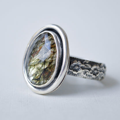 A sterling silver ring featuring an oval-cut gemstone with a shimmering gold, green, and blue iridescent play-of-color, set on a textured, hand-hammered silver band.