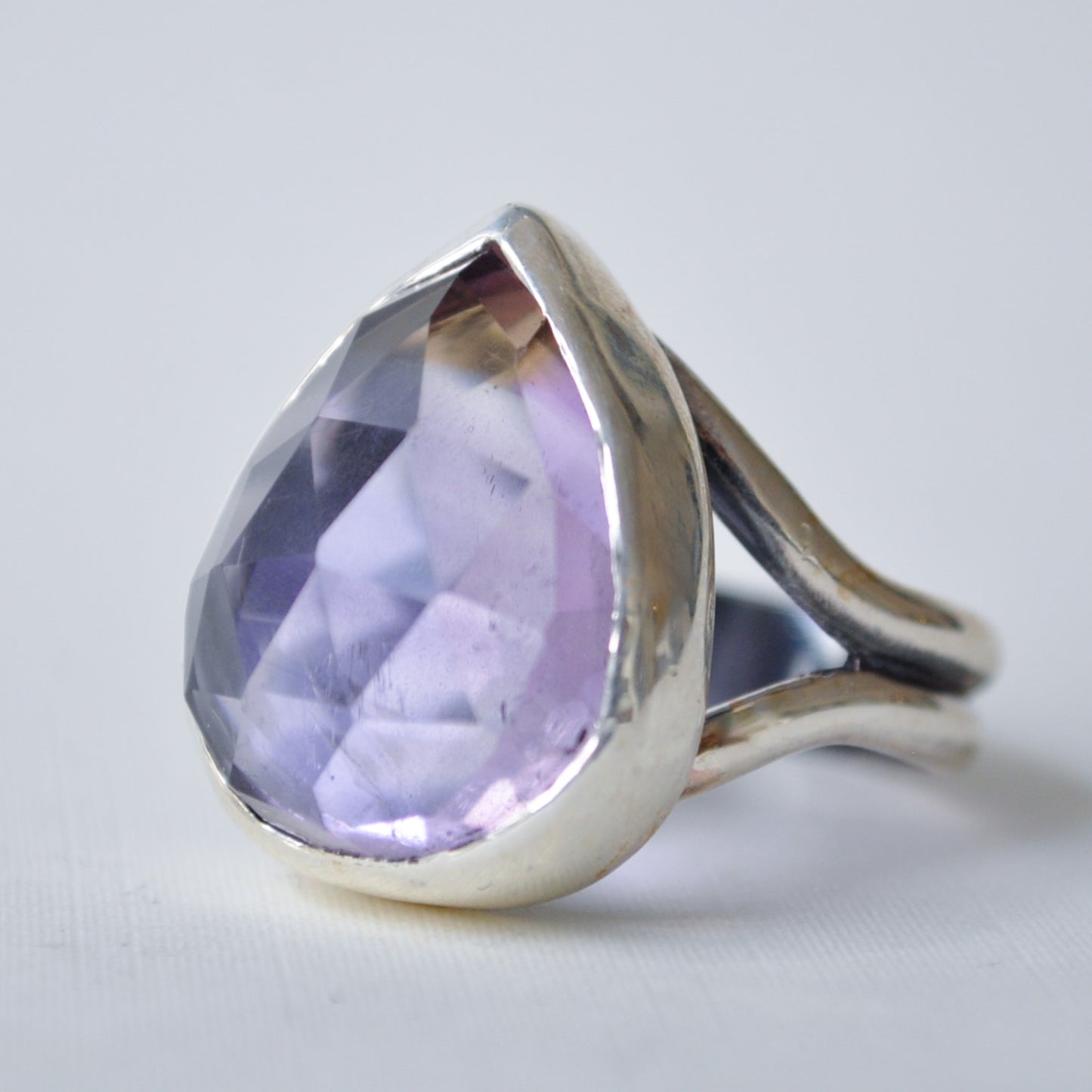 A silver ring featuring a large, faceted teardrop-shaped light purple gemstone, set against a plain light gray background.