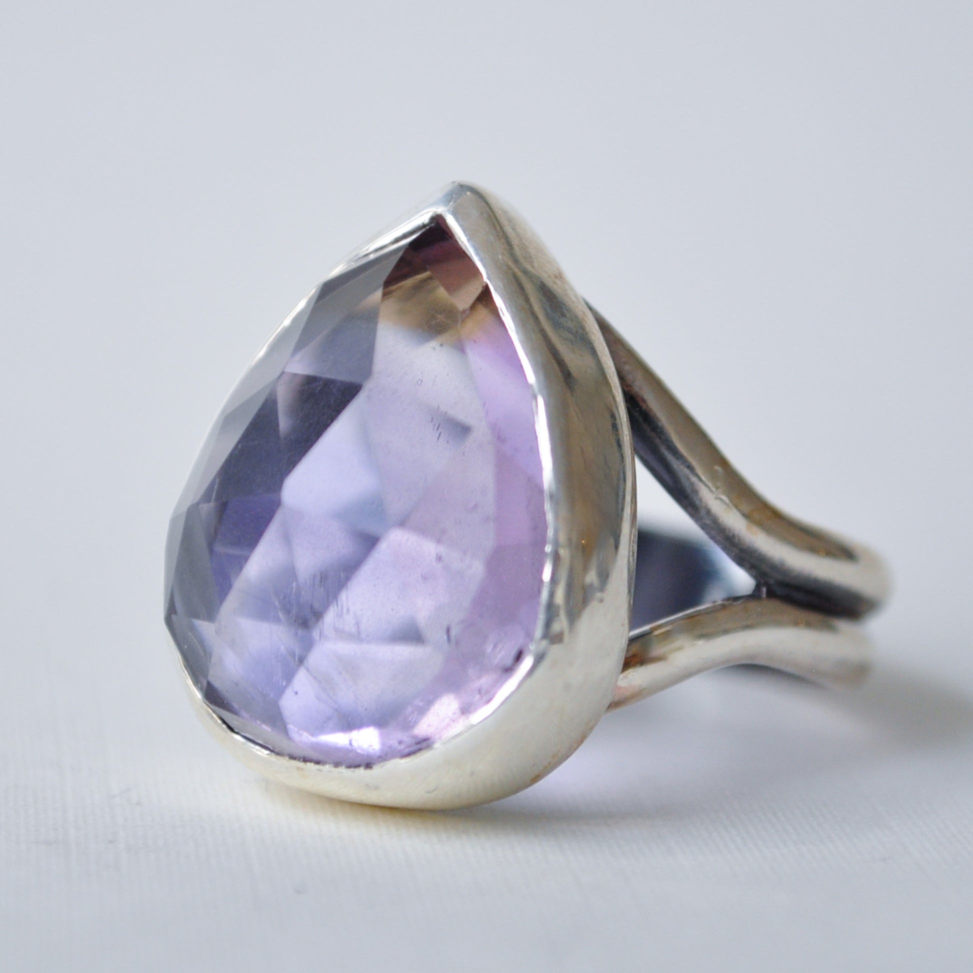 A silver ring featuring a large, faceted teardrop-shaped light purple gemstone, set against a plain light gray background.