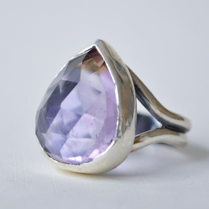 A silver ring featuring a large, faceted teardrop-shaped light purple gemstone, set against a plain light gray background.